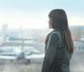 Mulher em um aeroporto olhando pela janela enquanto aviões estão estacionados.