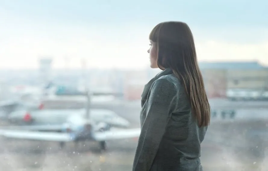 Como a Skycop ajuda passageiros a receber indenização por cancelamento rápido e seguro Mulher em um aeroporto olhando pela janela enquanto aviões estão estacionados.