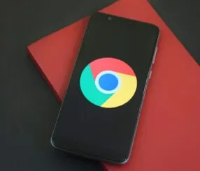 Como Ver e Desativar os Anúncios Personalizados do Google pelo Celular de Forma Simples e Rápida Um smartphone preto com o logo do Google Chrome sobre um fundo preto e vermelho.