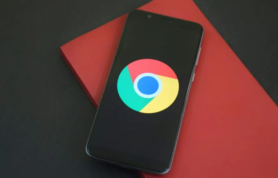 Como Ver e Desativar os Anúncios Personalizados do Google pelo Celular de Forma Simples e Rápida Um smartphone preto com o logo do Google Chrome sobre um fundo preto e vermelho.