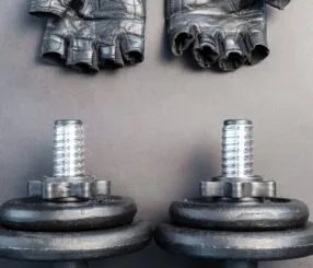 Halteres pretos e luvas de musculação sobre fundo escuro.