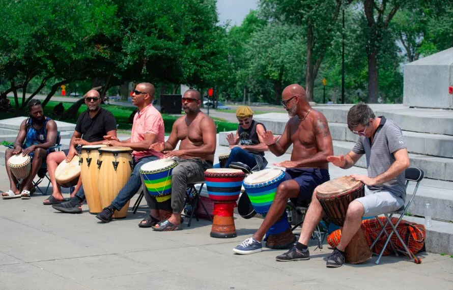 Como a musicalização ajuda adultos a aprender música do zero Grupo de adultos de diferentes idades tocando djembês e tambores numa roda de percussão ao ar livre em um parque